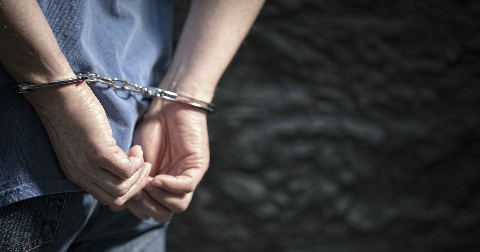 Einem jungen Mann sind die Hände mit Handschellen fixiert.