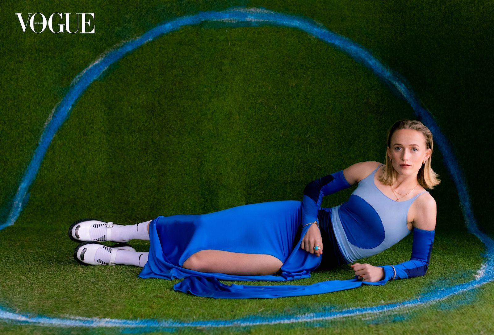 Lea Schüller in einem blauen Kleid auf dem Rasen liegend.