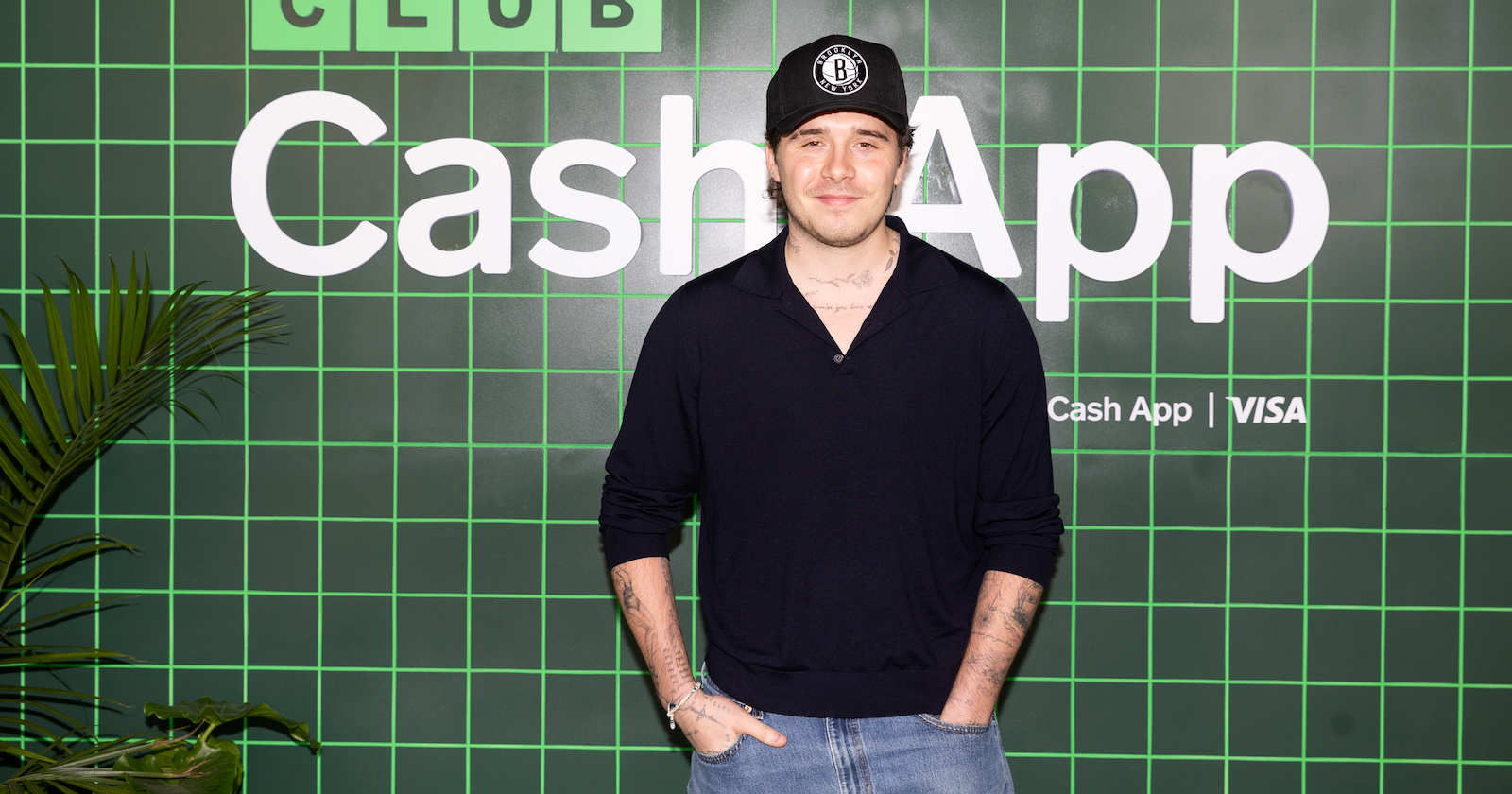 Brooklyn Beckham mit schwarzem Sweater und schwarzem Baseball-Cap.