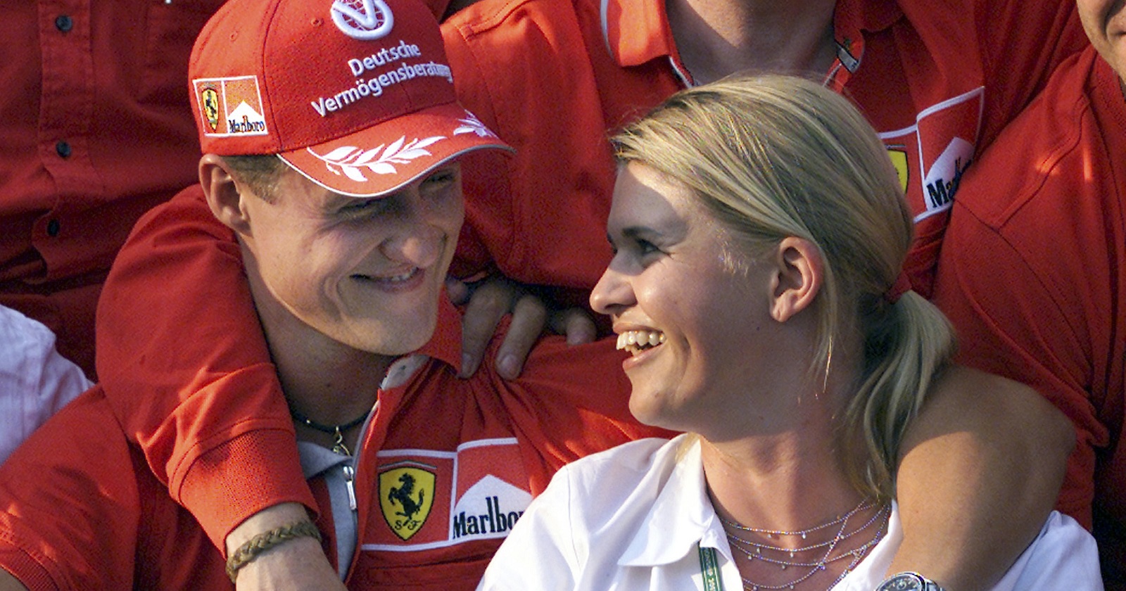 Michael und Corinna Schumacher sitzen Arm in Arm nebeneinander und schauen sich verliebt an.