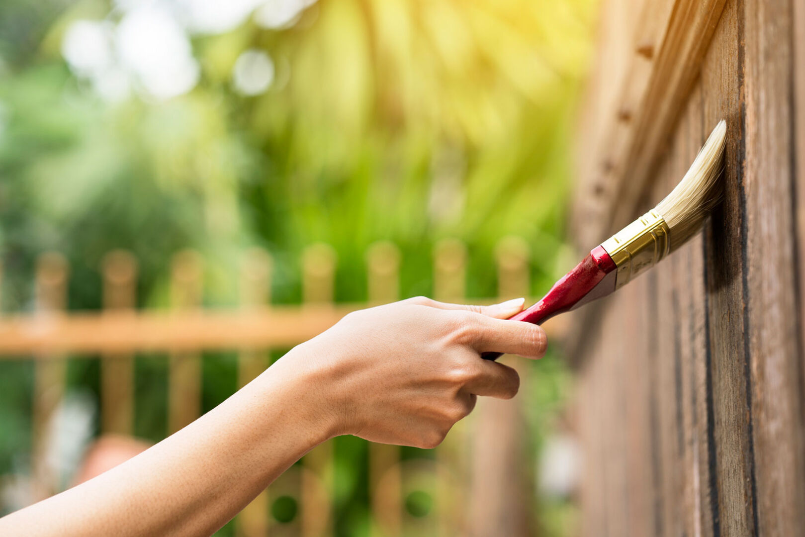 Frau streicht im Garten ihren Holzzaun | iStock.com/Tatomm