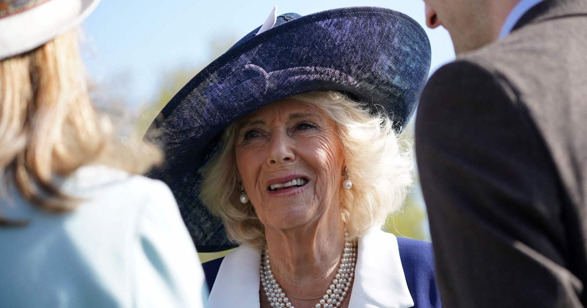 Camilla mit blauem Kostüm und Hut.