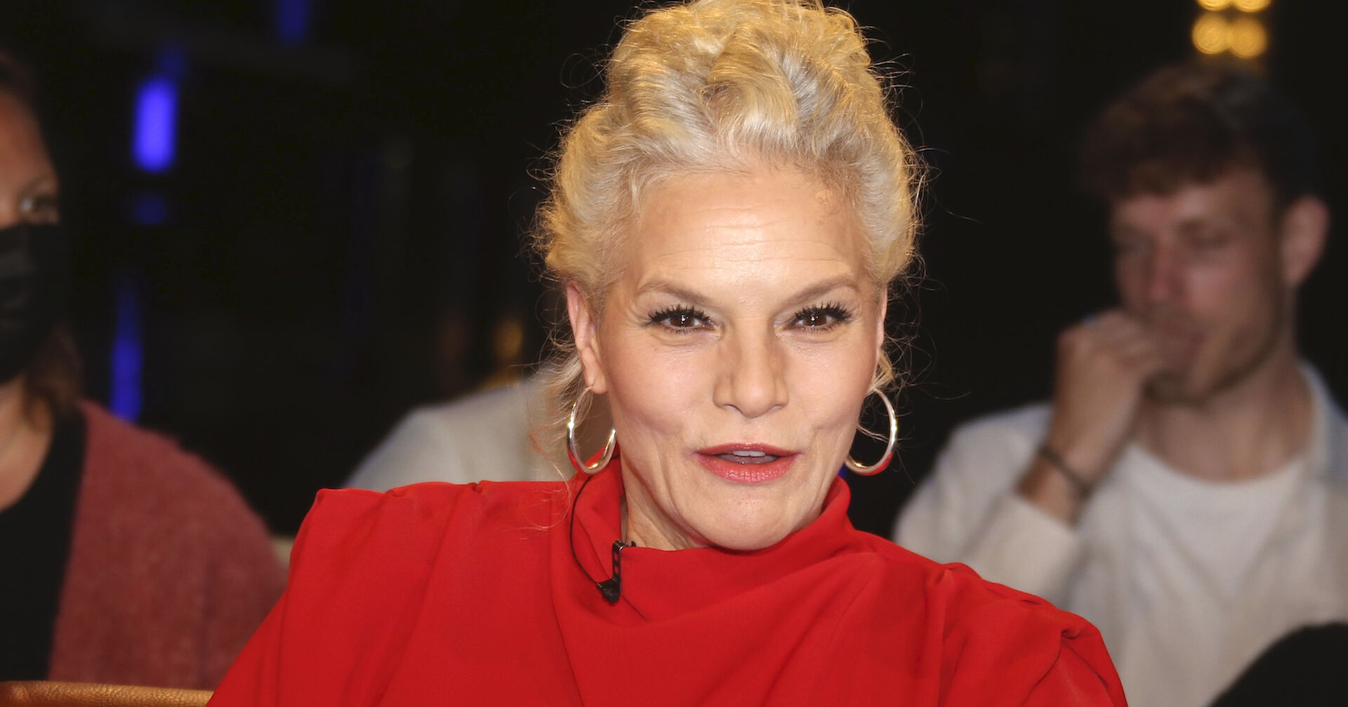 Ina Müller in einem roten Kleid mit großen Ohrringen.