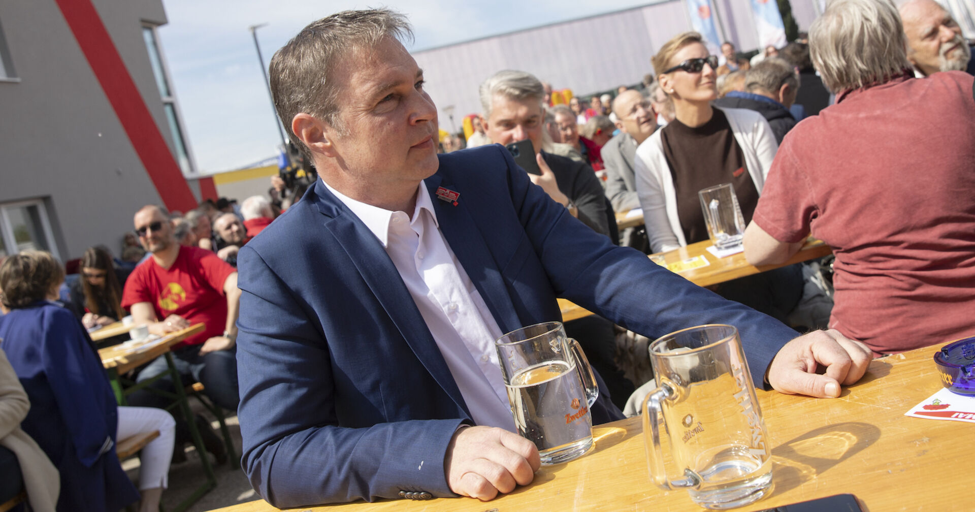 Andi Babler sitzt an einer Bierbank im Freien, hinter ihm Menschen. Vor ihm steht ein großer Spritzer