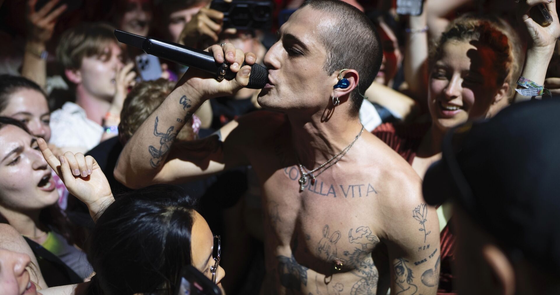 Ein tätowierter Mann mit Glatze singt in ein Mikrophon umringt von Fans.