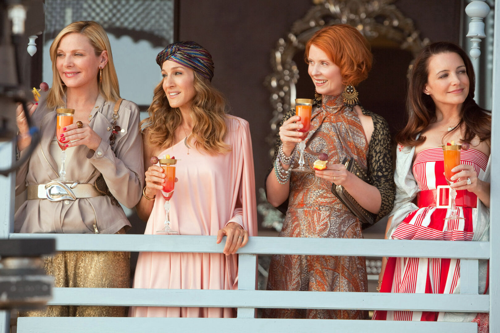 Szene aus dem Film Sex and the City 2, vier Frauen stehen auf einem Balkon und trinken aus einem Sektglas.