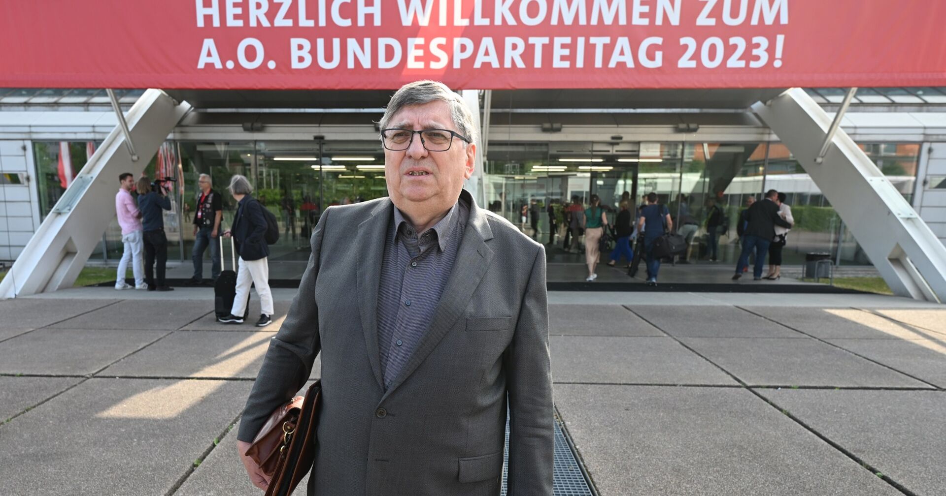 Berthold Felber mit Aktentasche vor dem Eingang des Linzer Designcenters. Über dem Eingang ist ein Transparent mit dem Wortlaut "Herzlich willkommen zum A.O. Bundesparteitag 2023!