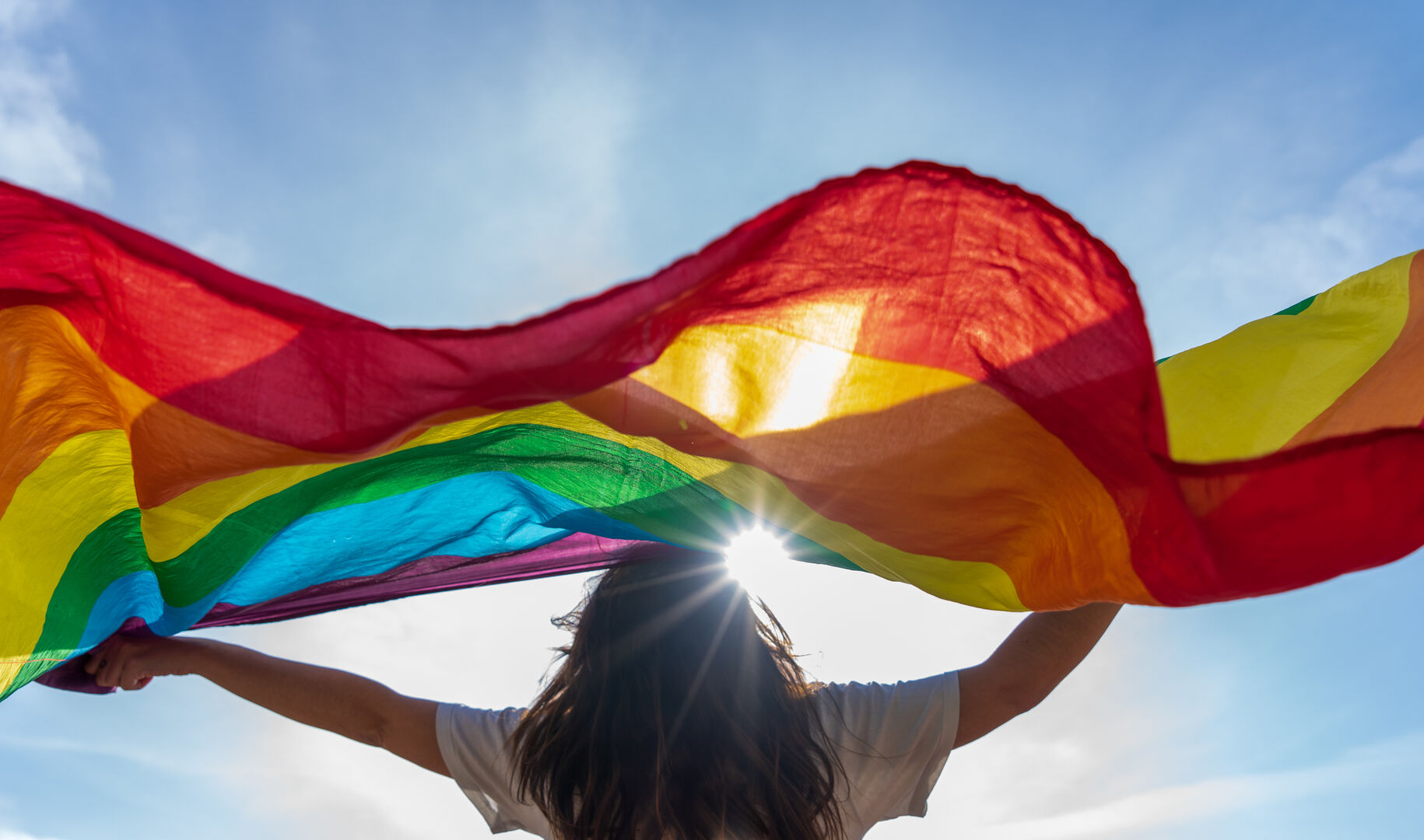 Frau hält Regenbogenflagge hoch in die Luft