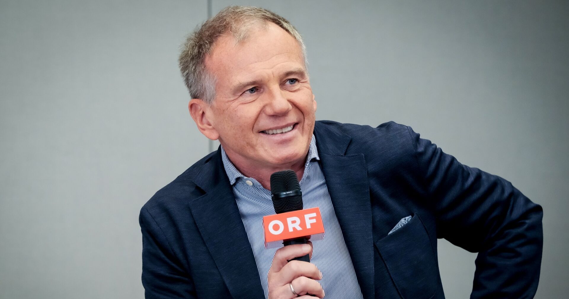Armin Wolf ist im Gespräch, er lächelt und hält ein ORF-Mikrofon in der Hand.