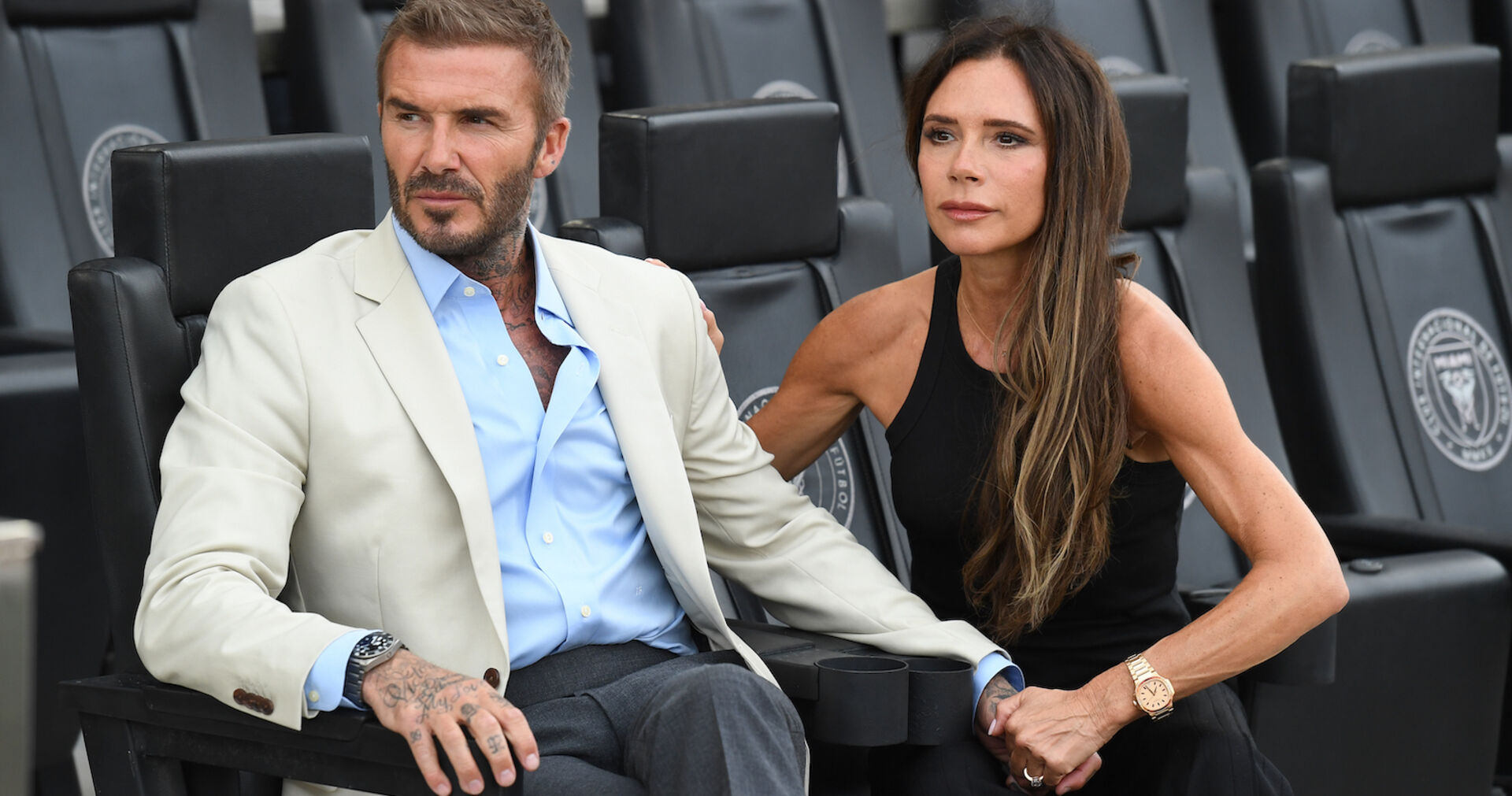 Ein Mann im beigen Sakko sitzt neben einer dünnen Frau in einem schwarzen Top.