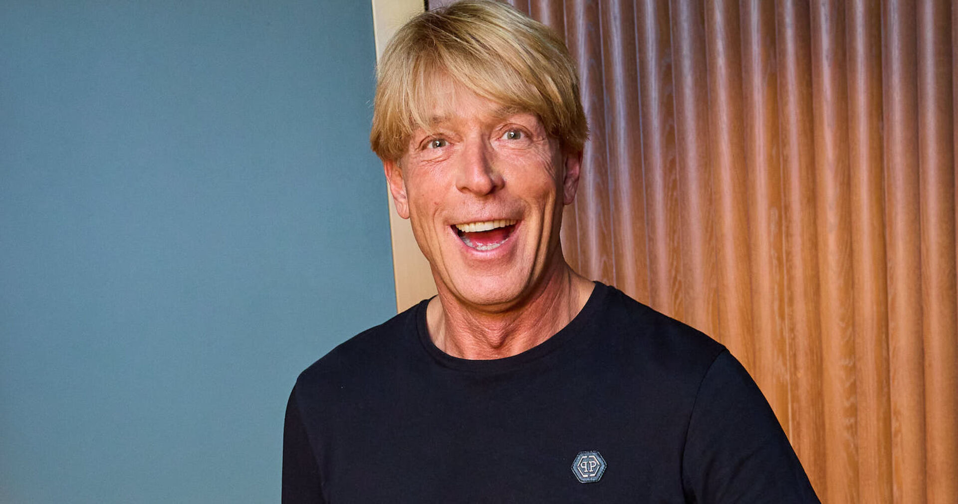 Ein Mann mit blonden Haaren lacht in die Kamera.