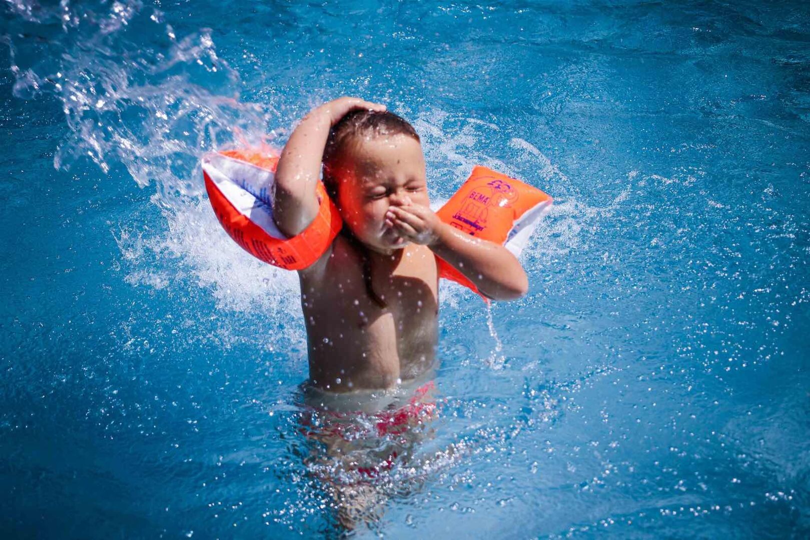Kleinkind mit orangen "Schwimm-Flügerln" im Becken.