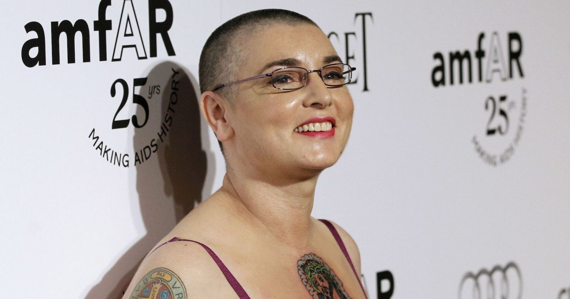 Sinéad O'Connor lächelnd mit kurzen Haaren und Brille.