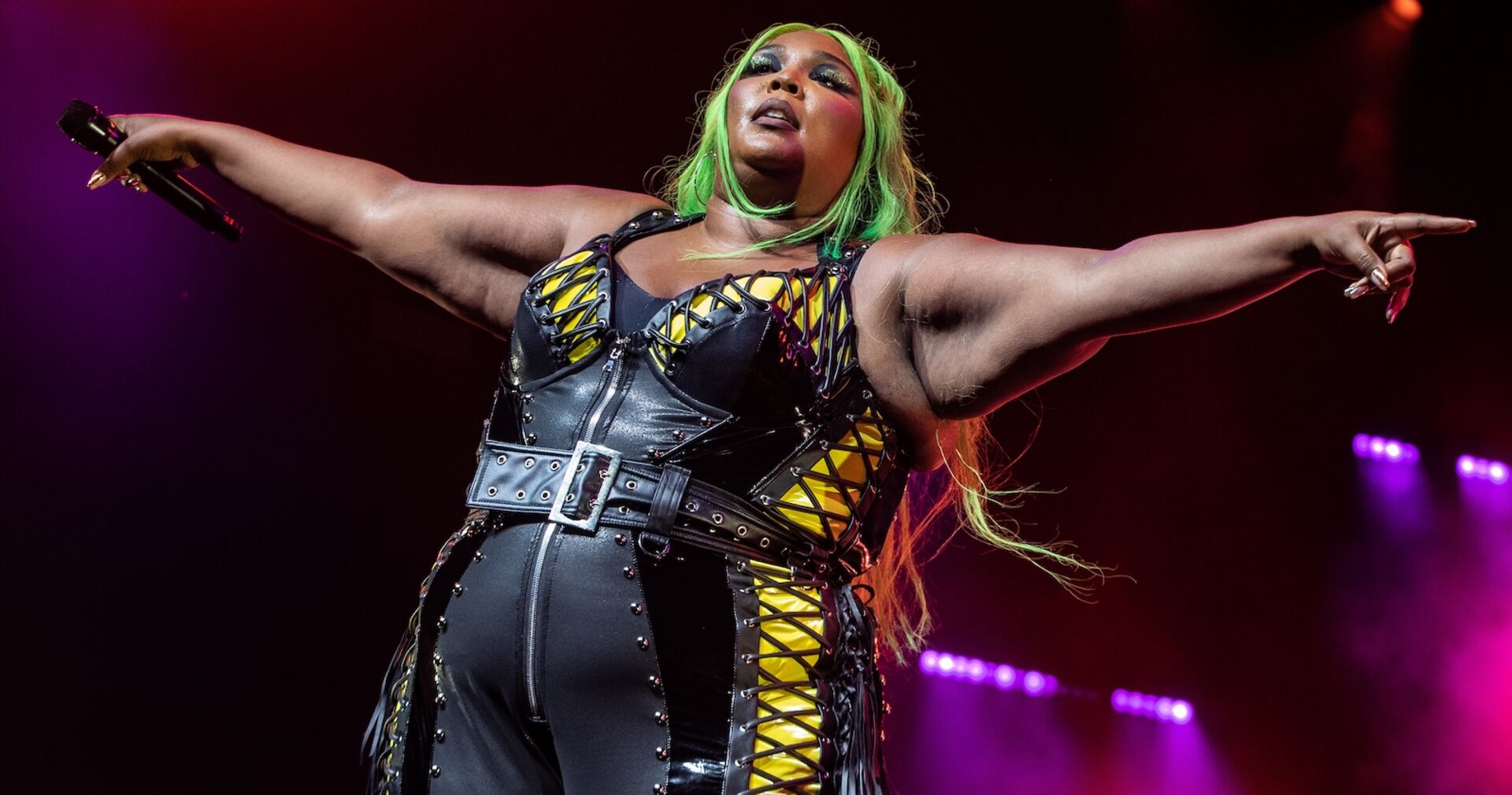 Eine dicke schwarze Frau mit grünen Haaren steht auf der Bühne.