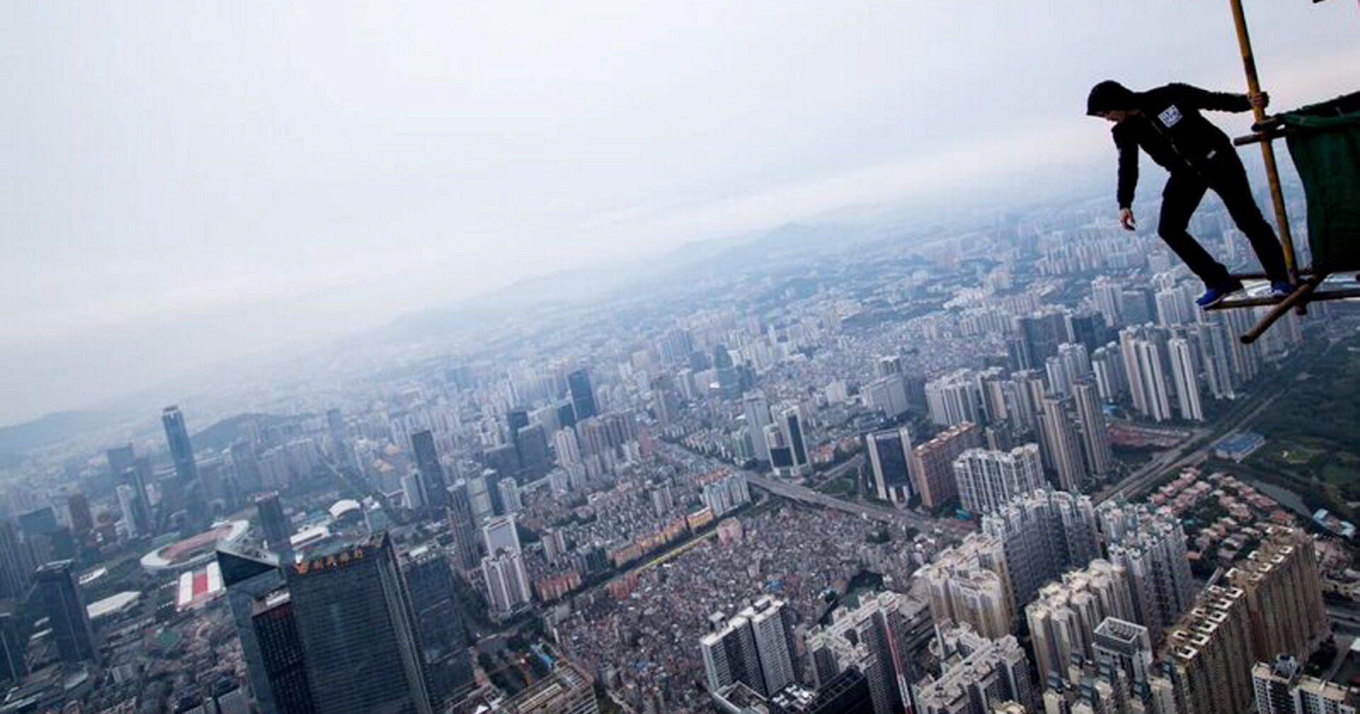 Mann steht in schwindelerregender Höhe auf einem Wolkenkratzer.