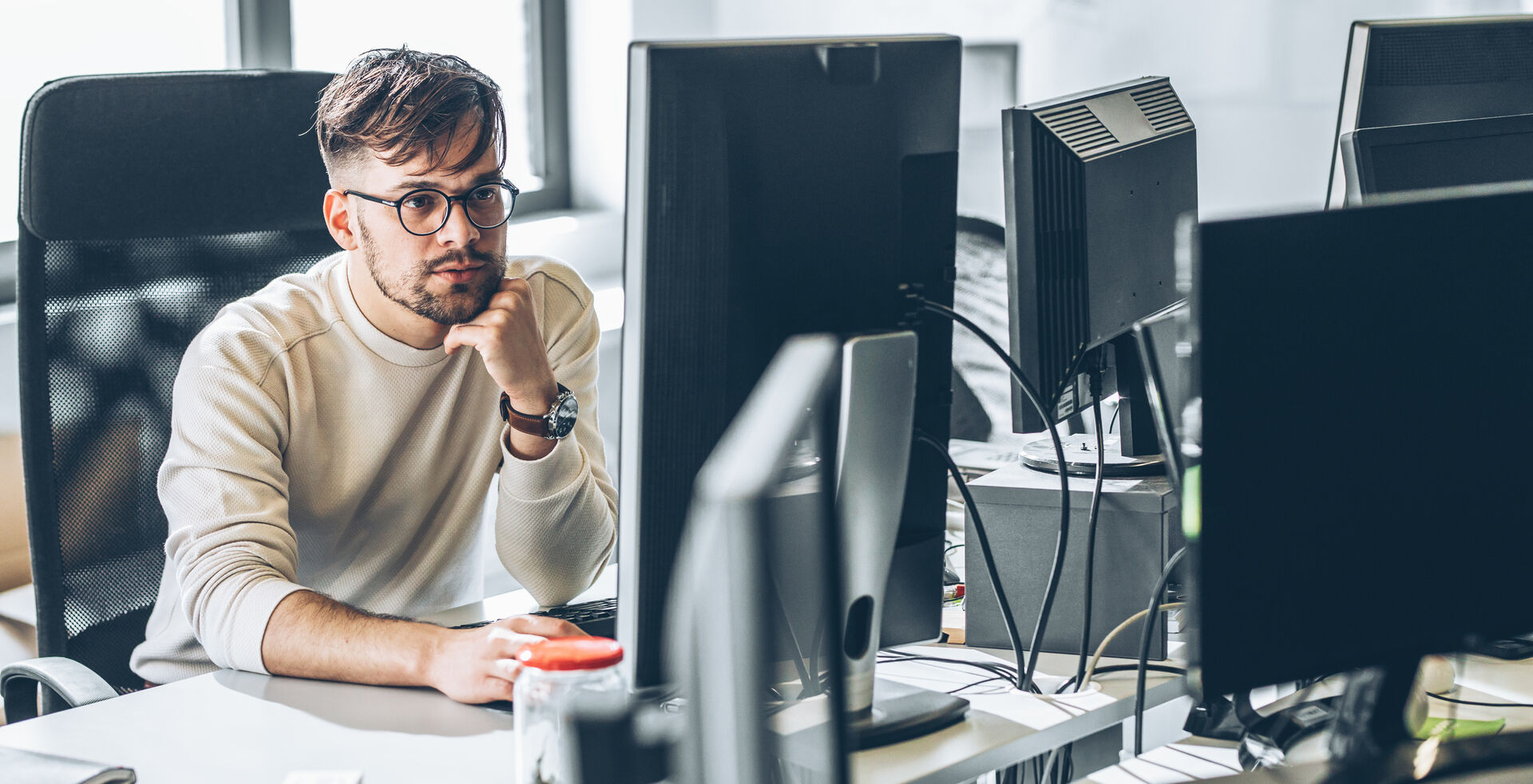 Junger Mann nachdenkend vor zwei Computerbildschirmen