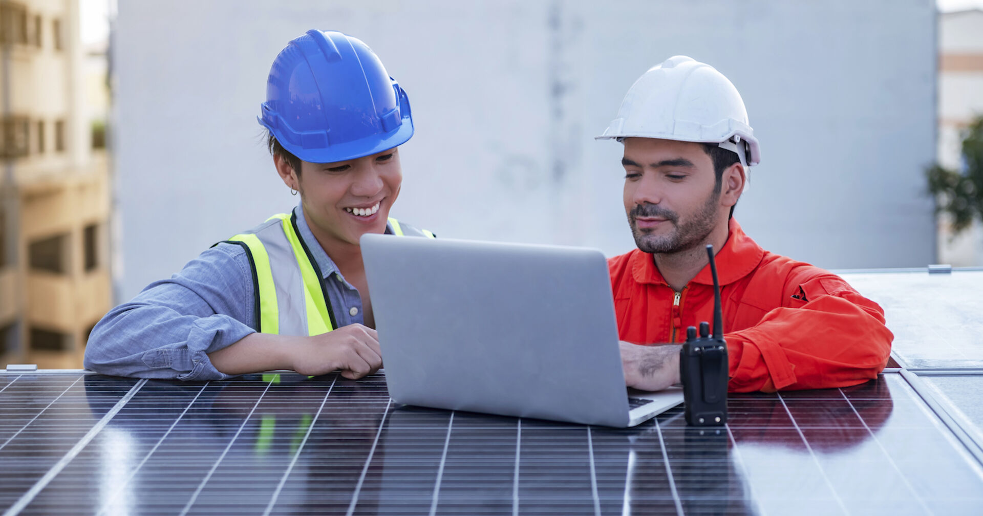 Zwei Arbeiter stehen vor einem Solarpaneel und schauen in einen Laptop
