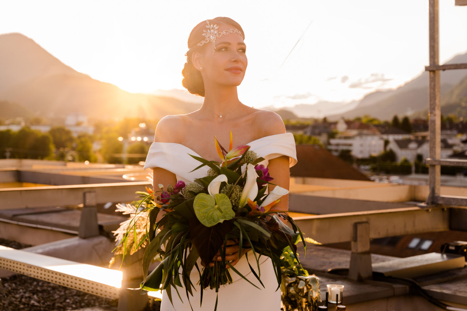 Junge Frau steht bei Sonnenuntergang im Brautkleid mit Blumen in den Händen
