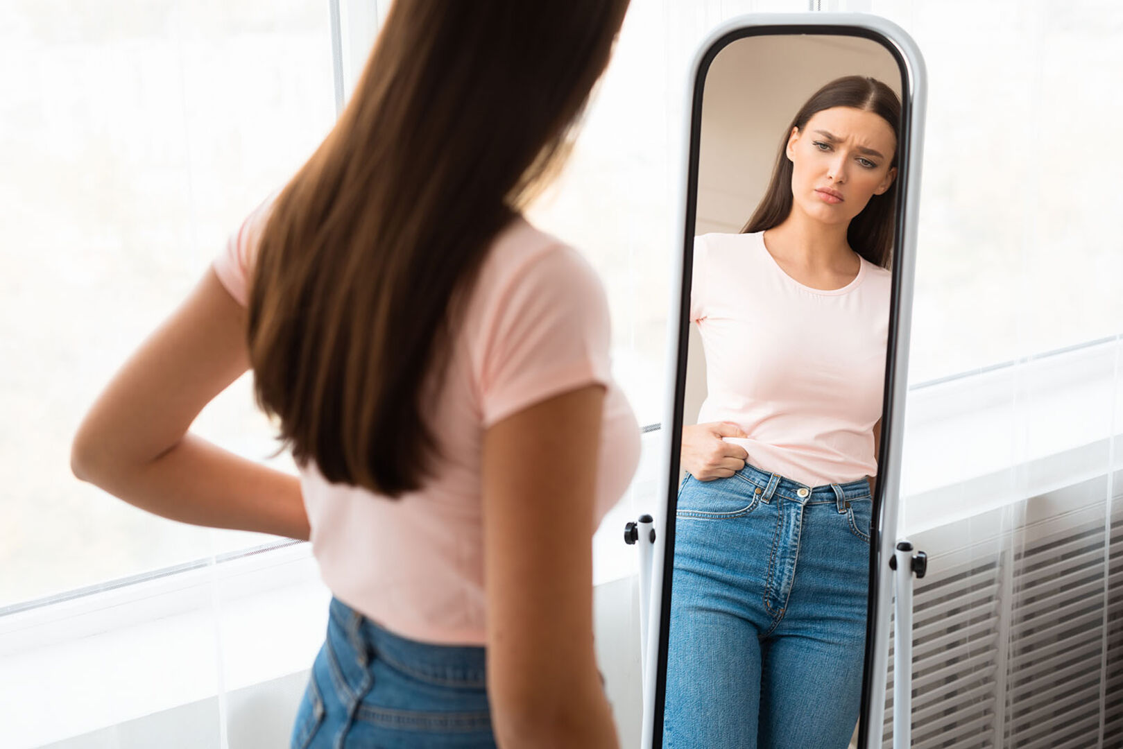 Frau steht vor Spiegel und betrachtet ihren Bauch | Credit: iStock.com/Prostock-Studio