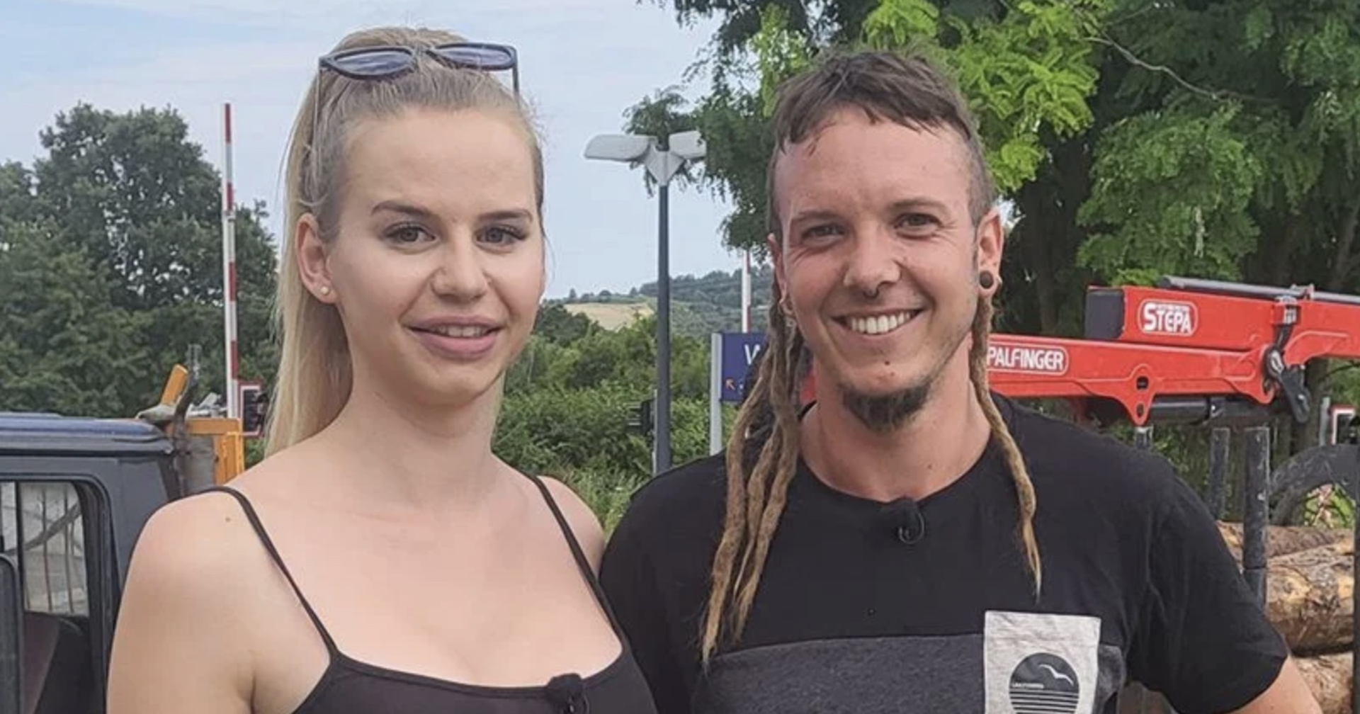 Eine blonde Frau und ein Mann mit Dreadlocks am Land vor einem Traktor.