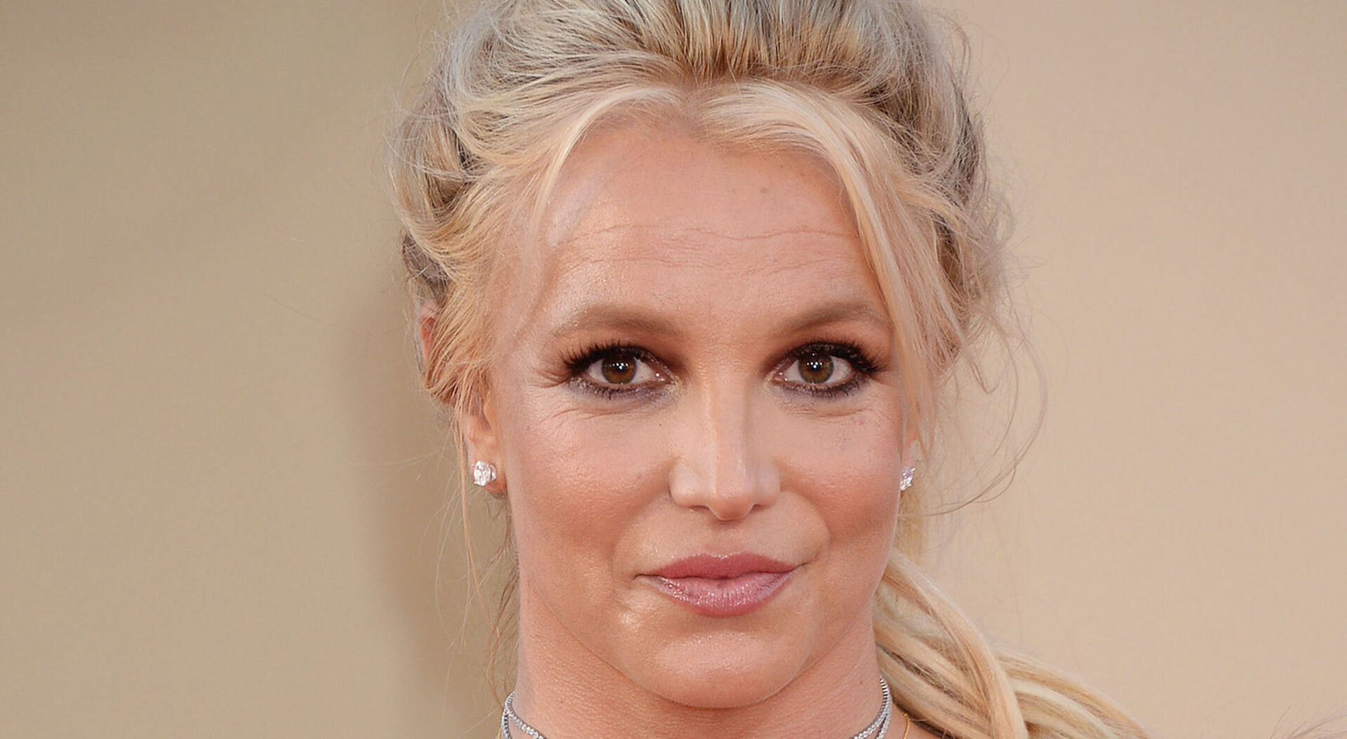 Britney Spears mit geschlossenen langen blonden Haaren vor einer Fotoleinwand