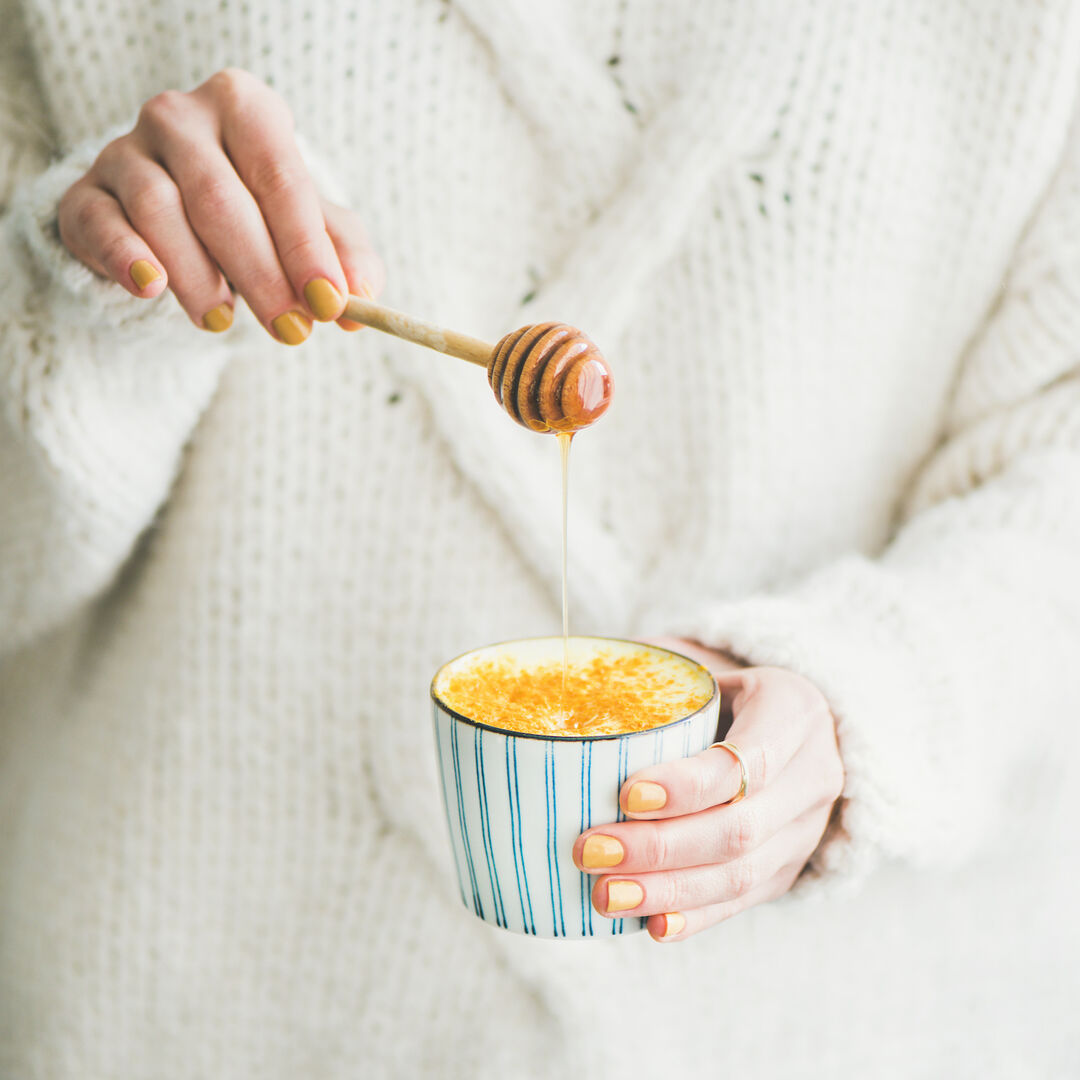Golden Milk in der Tasse, Frau fügt Honig hinzu