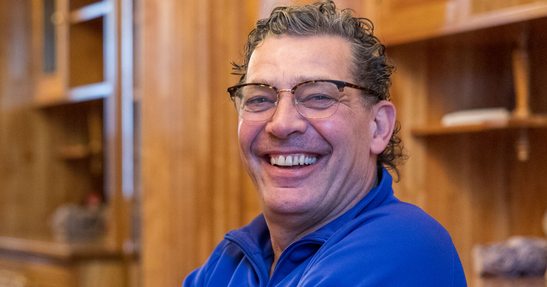 Schauspieler Gregor Blóeb mit einem blauen Hemd vor einer Holzwand.