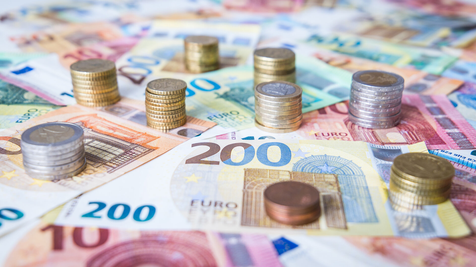 Ein Teppich aus ausgebreiteten Euro-Geldscheinen, auf denen sich neun Euro-Münzentürme erheben