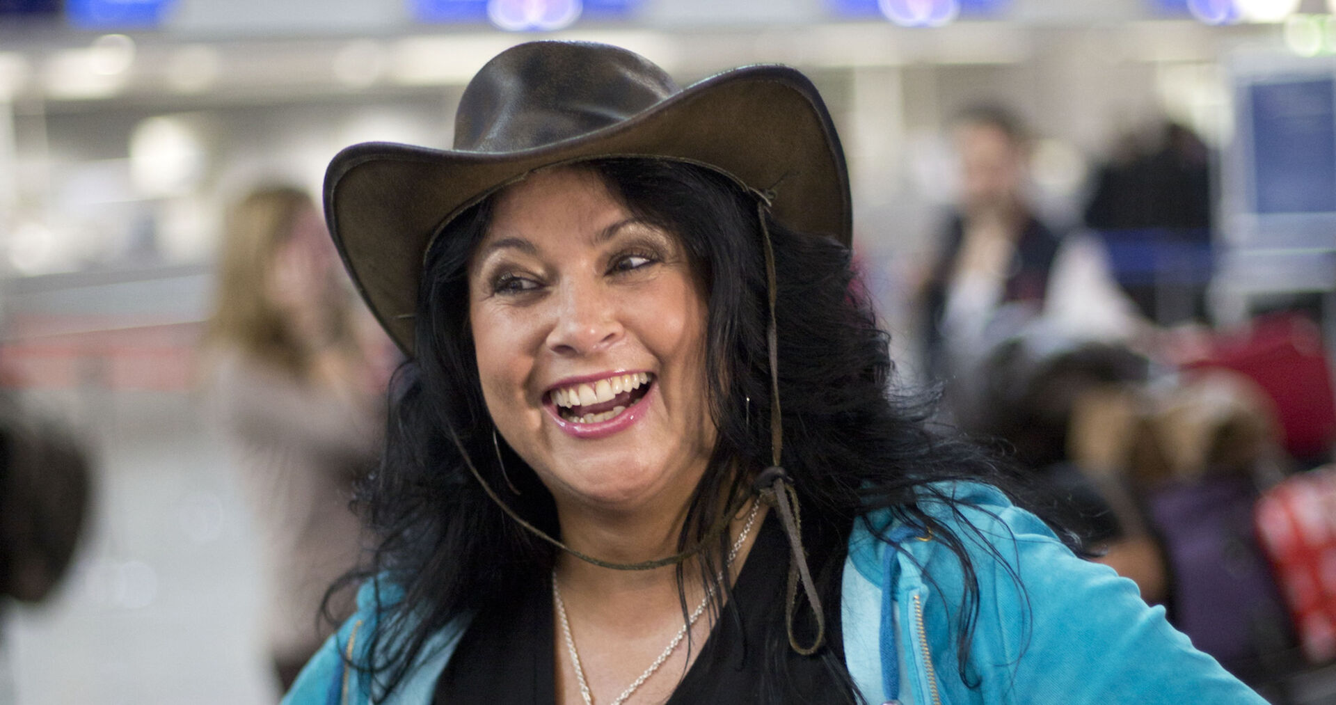 Iris Klein mit einer blauen Weste und einem braunen Cowboyhut auf einem Flughafen.
