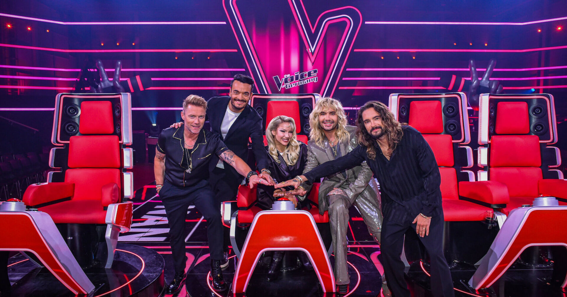 The Voice of Germany Jury vor vier roten Jurystühlen und im Hintergrund ein großes Voice of Germany Logo