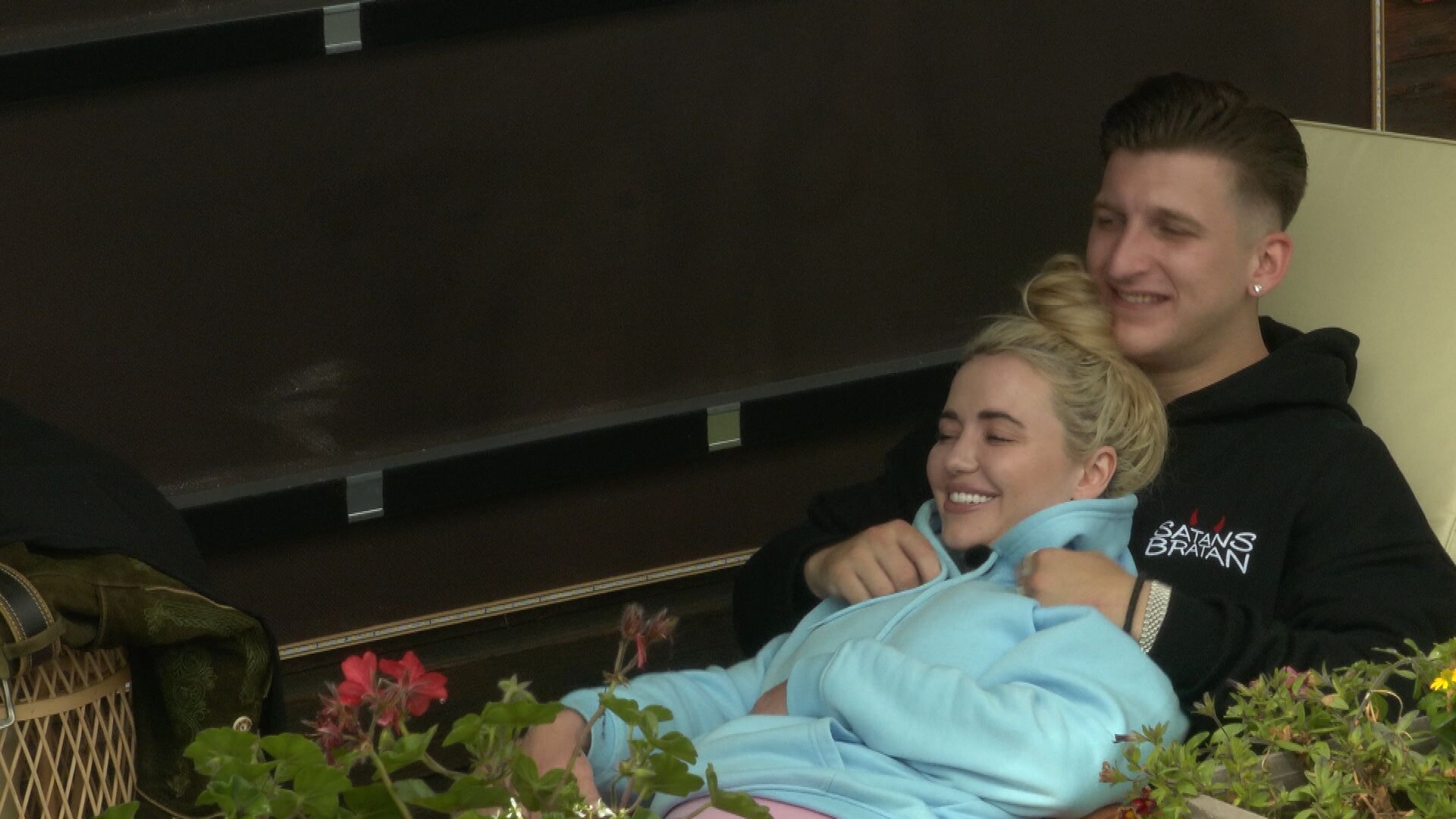 Cathy Lugner kuschelt mit Eric auf einer Liege. Sie trägt einen hellblauen Pullover und er einen schwarzen Hoodie.