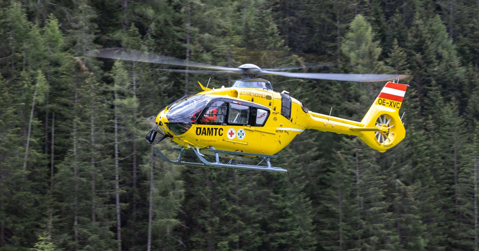 Der gelbe ÖAMTC-Hubschrauber fliegt in einem Waldgebiet.