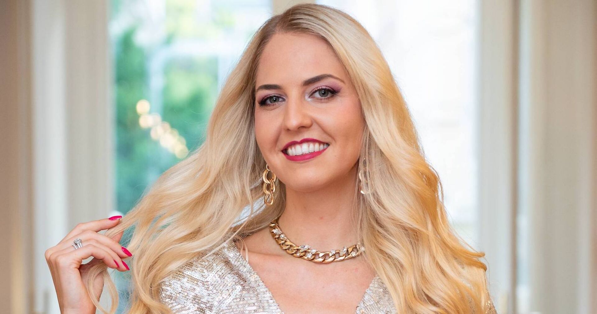 Beatrice Turin mit langen blonden gewellten Haaren vor einem großen Fenster.