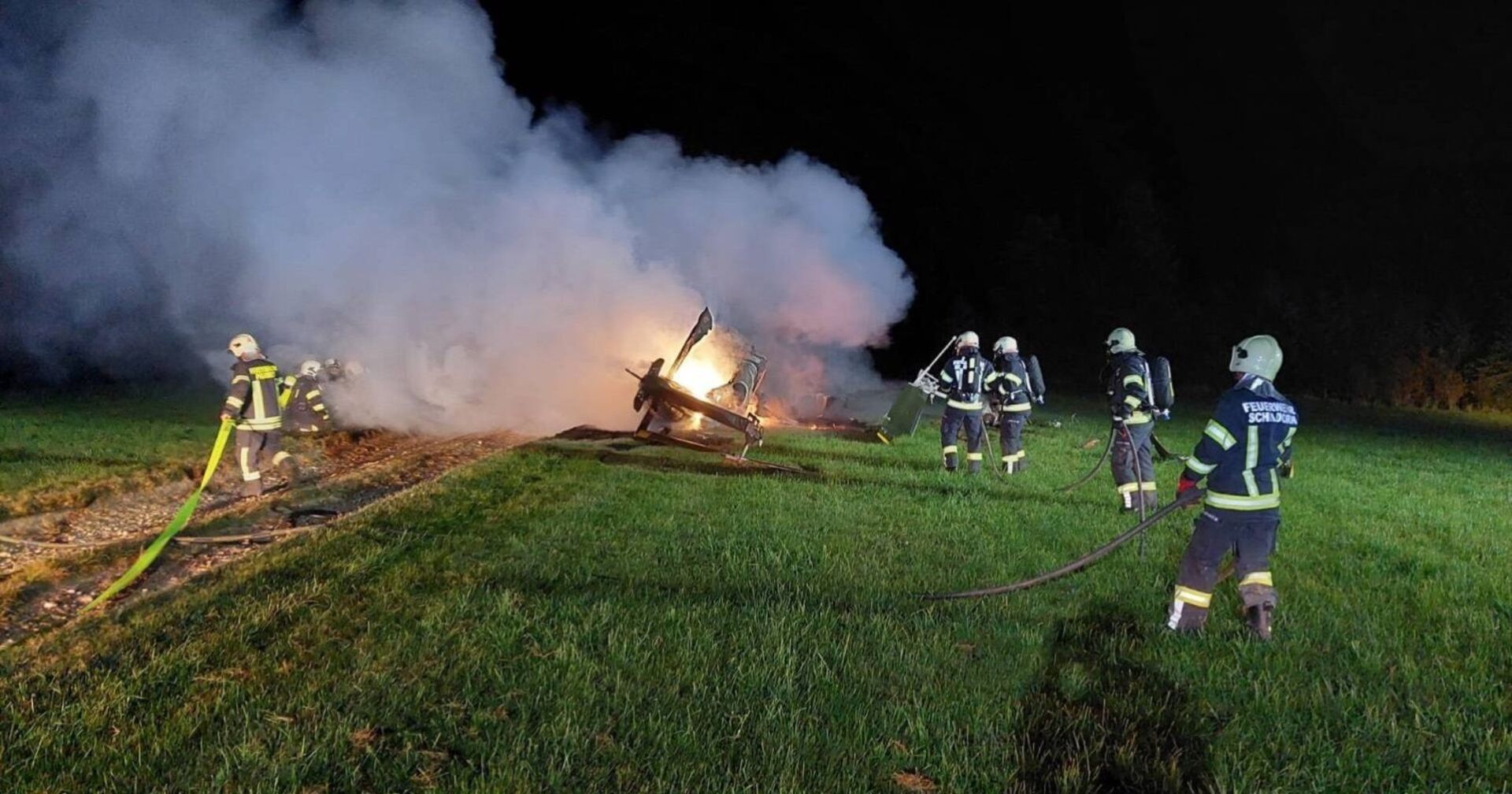 Feuerwehrmänner versuchen einen brennenden Hubschrauber auf einem Feld zu löschen.