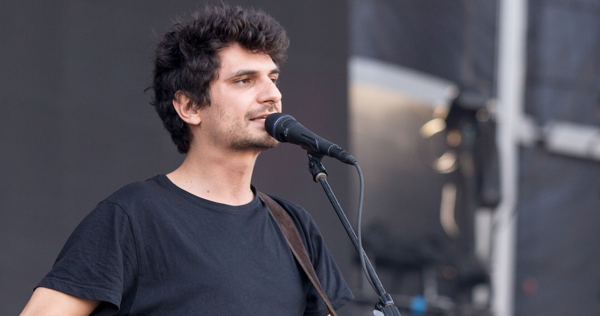 James Hersey steht mit kurzen schwarzen Haaren auf der Bühne und singt in ein Mikrofon.