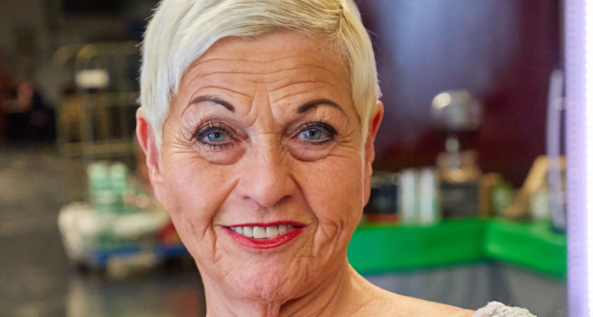 Eine Dame reifen Alters mit einem pinken Lippenstift und sehr kurzen blonden Haaren.