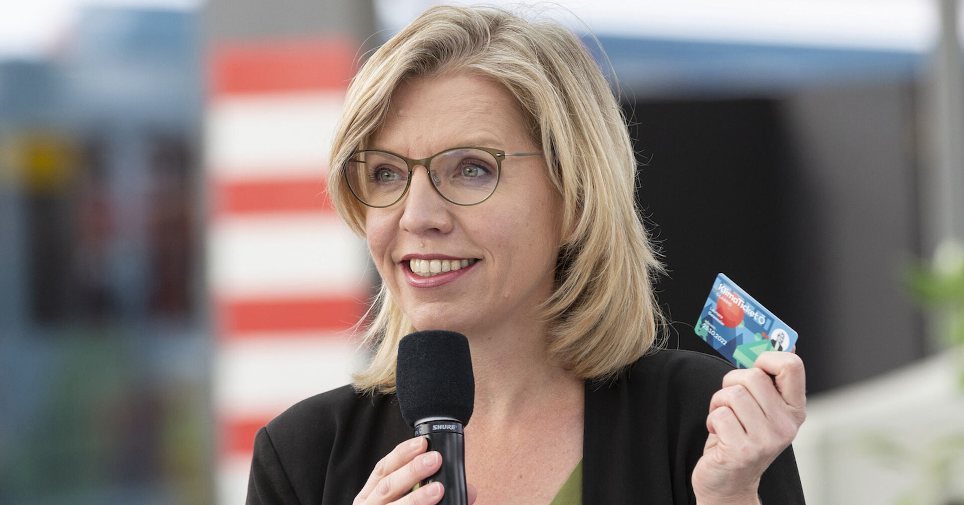 Gewessler hält ein Klimaticket hoch.