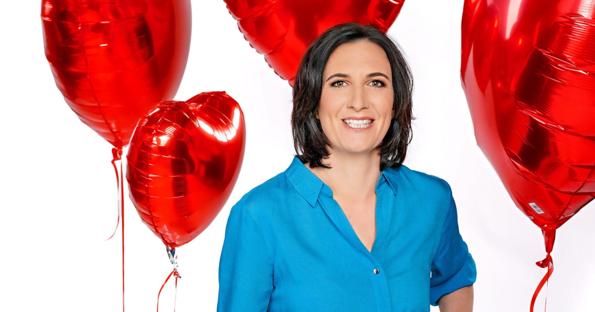 Nina Horowitz mit einem blauen Hemd vor Liebeslufballonen.