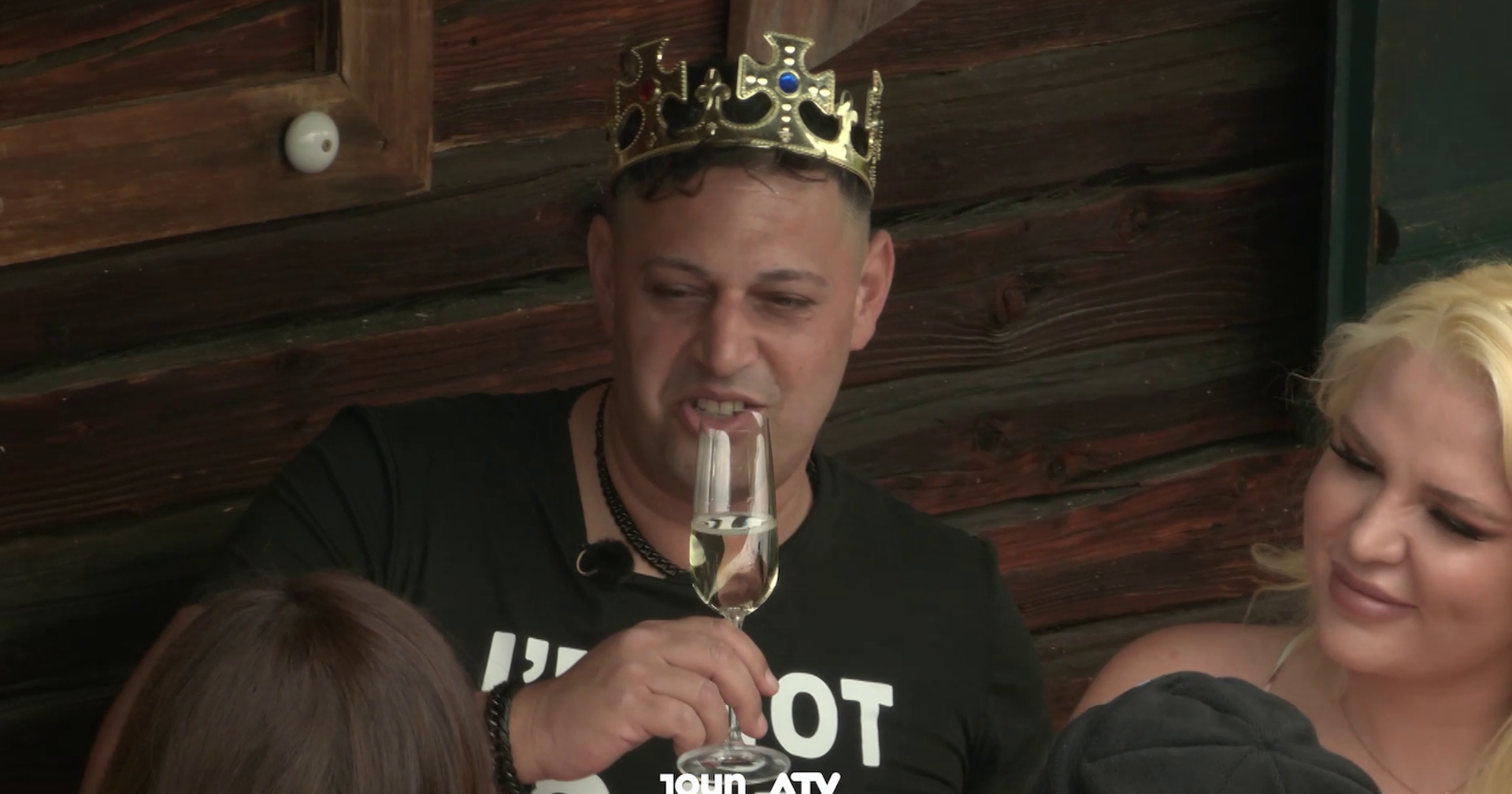 Forsthaus Rampensau Teilnehmer Marius mit einer Plastikkrone auf dem Kopf und einem Sektglas in der Hand.