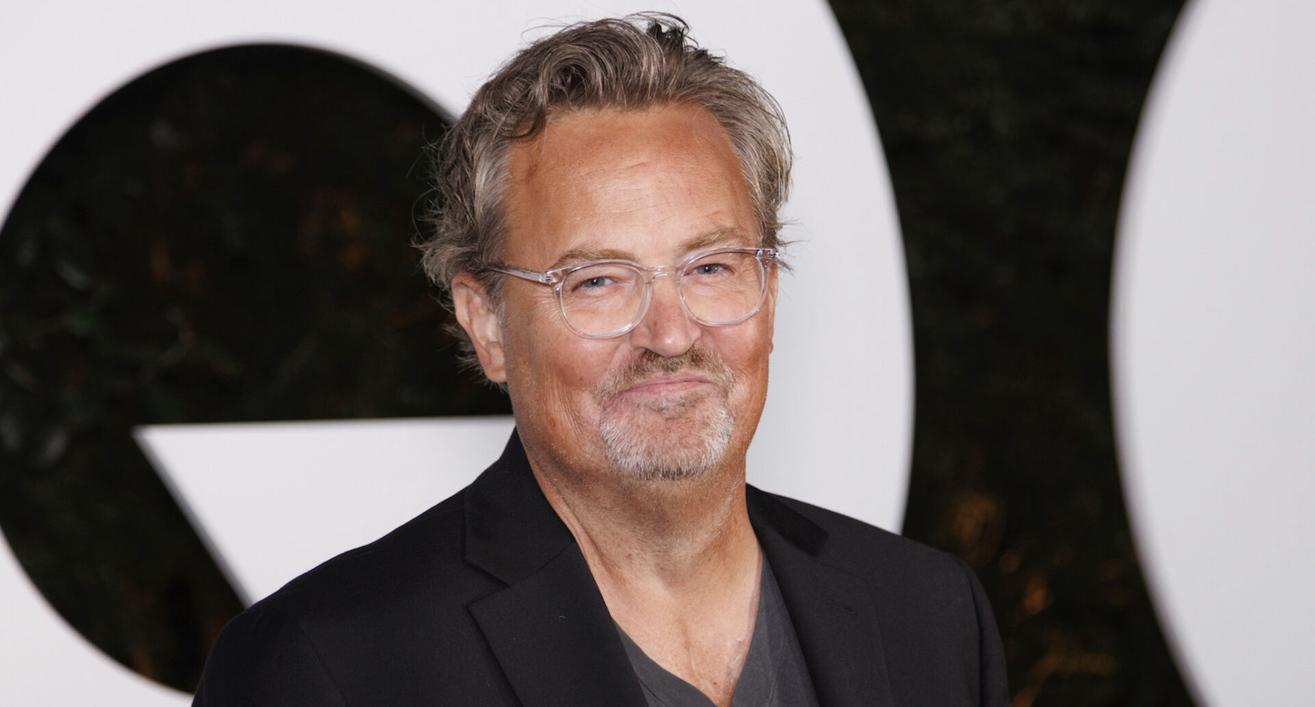 Matthew Perry beim CQ Award mit einem schwarzen Anzug und einer Brille.