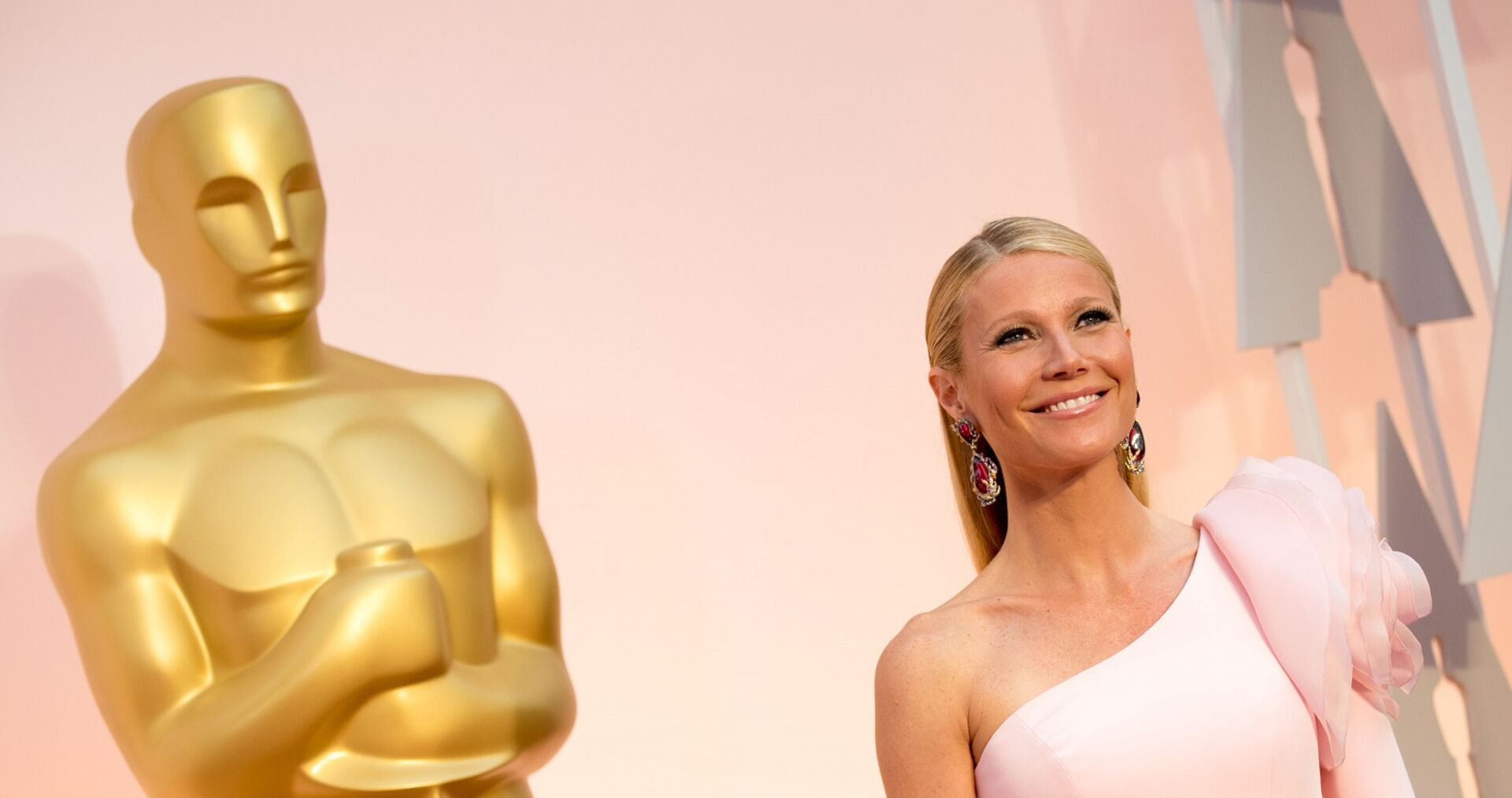Gwyneth Paltrow in einem rosa Kleid neben einer Oscarstatue