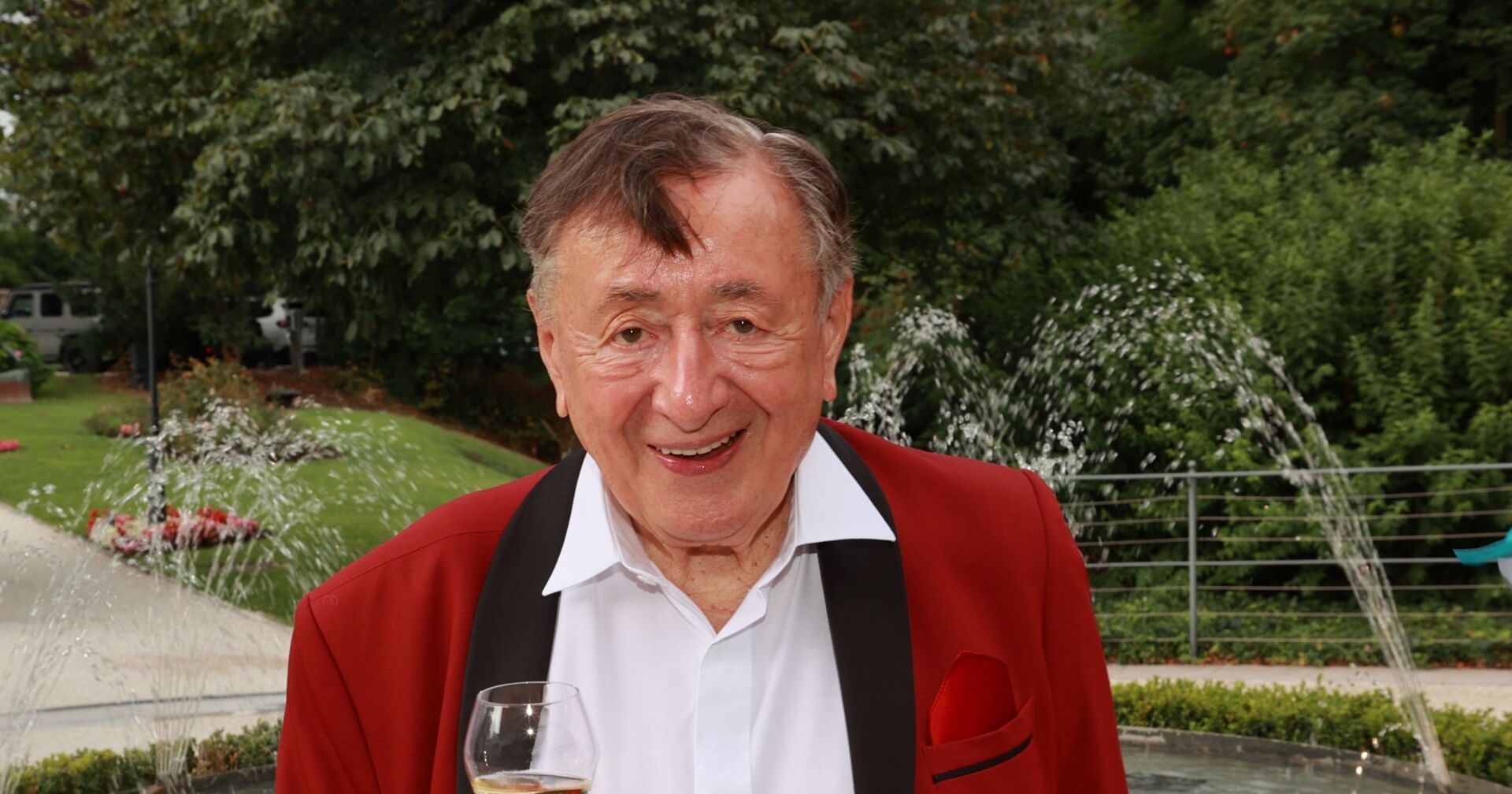 Richard Lugner vor einem Schlosspark mit rotem Anzug