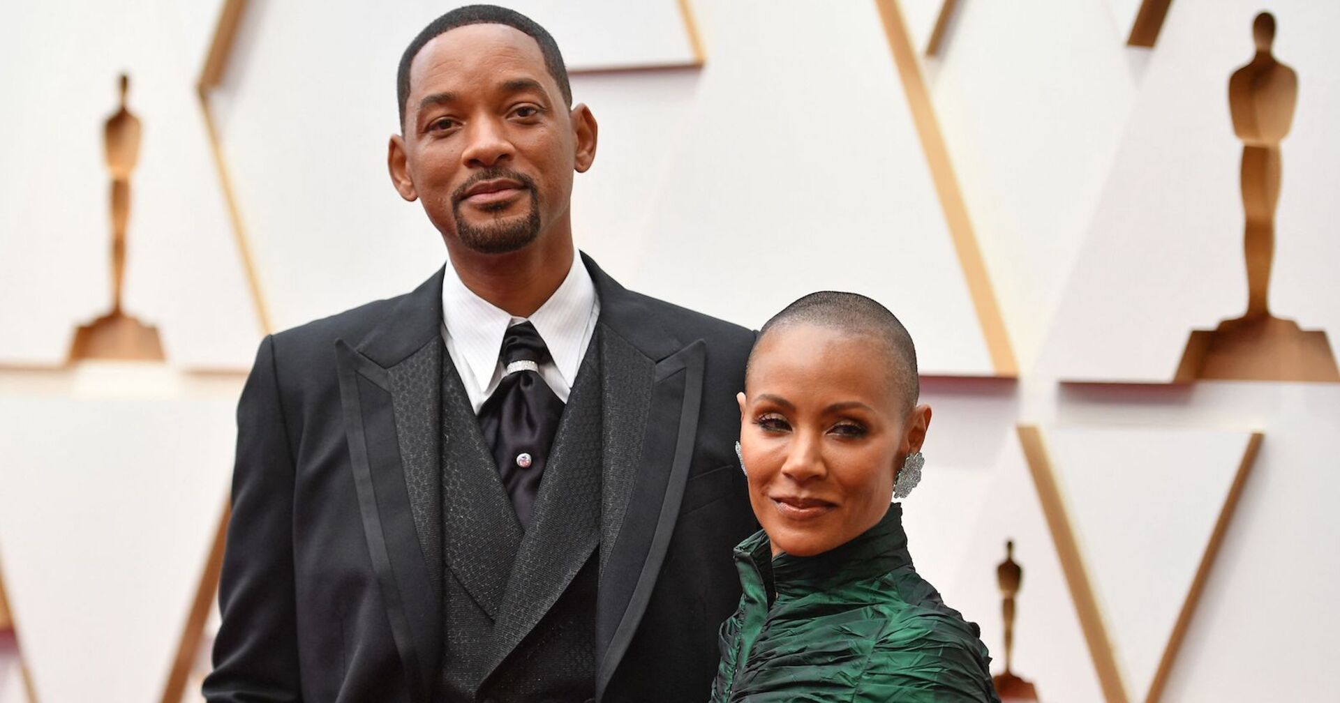 Will Smith trägt ein Sakko und Jada Smith ein hochgeschlossenes dunkelgrünes Kleid.