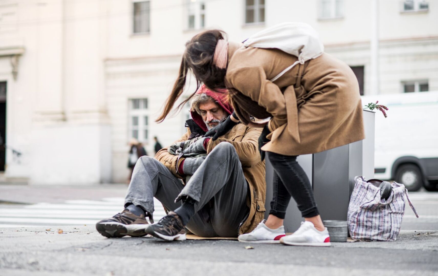 Eine Frau hilft einem Obdachlosen auf der Straße.