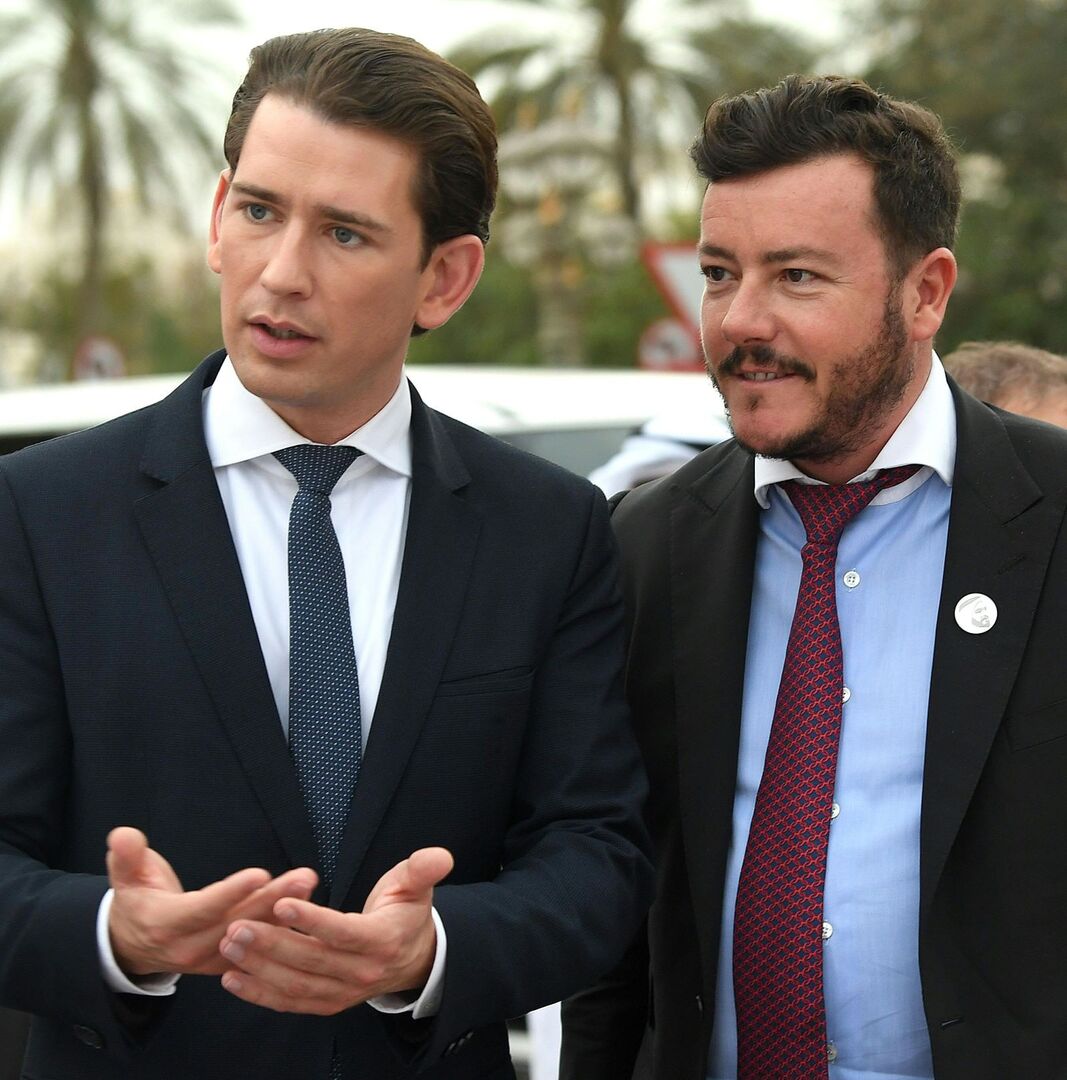 Sebastian Kurz und René Benko dicht Schulter an Schulter im Anzug mit Krawatte. Im Hintergrund Palmen