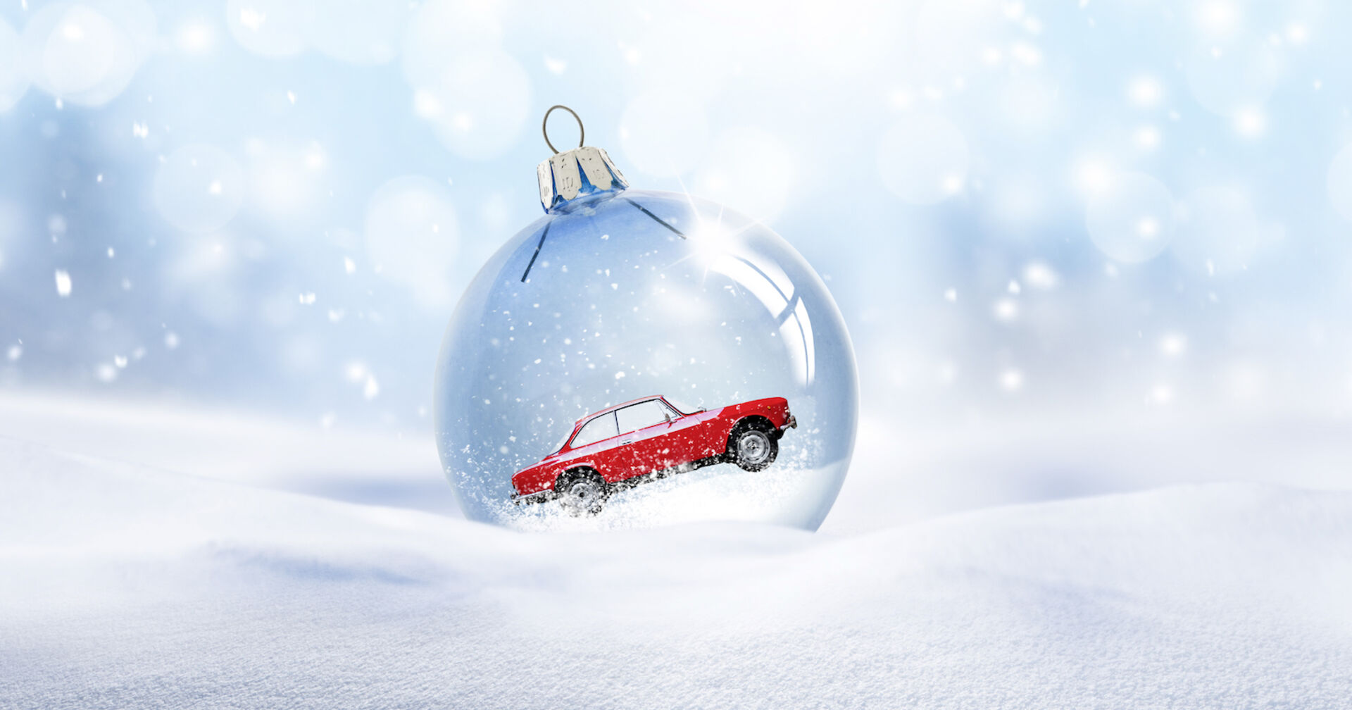 Modellauto in einer durchsichtigen Christbaumkugel, die auf einer Schneelandschaft liegt