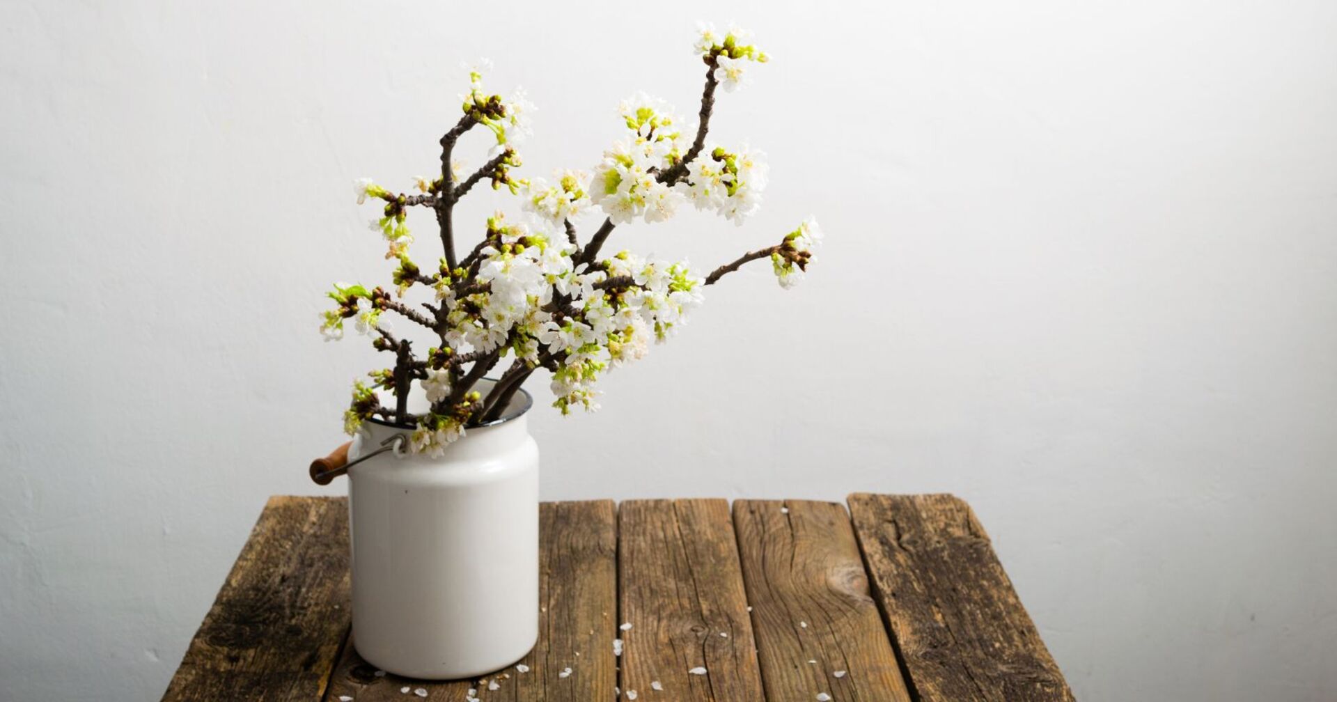 Barbarazweige stehen blühend in einer Vase auf einem Holztisch.
