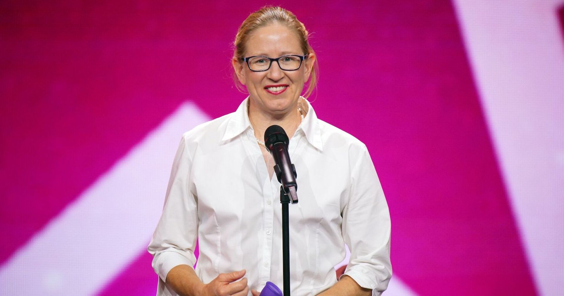 Die australische "Das Supertalent" Teilnehmerin Beatrice McQueef steht vor einem Mikrofon und trägt ein weißes Hemd. Hinter ihr ist eine pinke Fotowand.