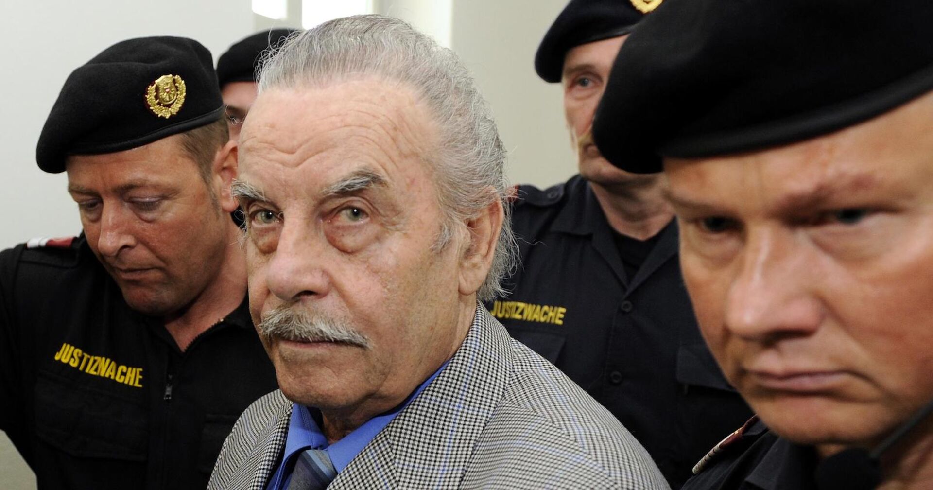 Josef Fritzl zwischen Polizisten am Weg ins Gericht. Er sieht direkt in die Kamera