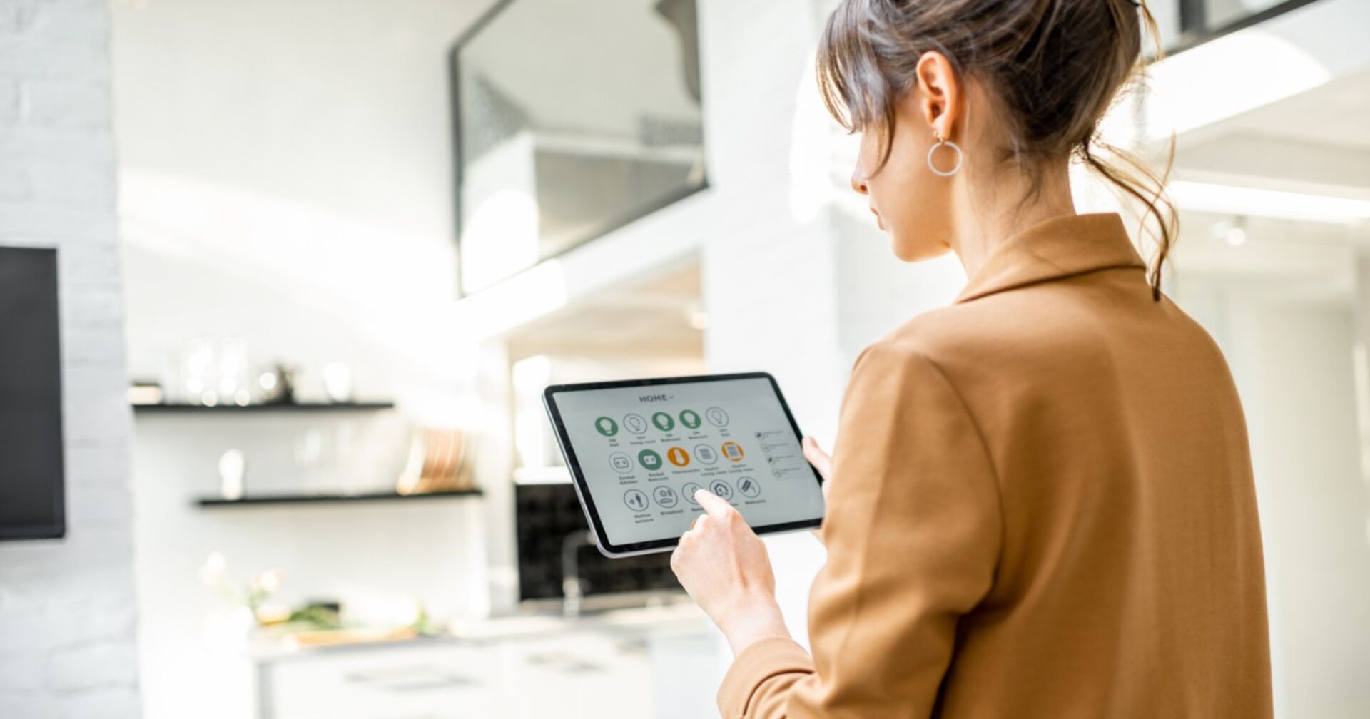 Frau steht in der Küche mit einem Tablet in der Hand, mit welchem sie unterschiedliche Bereiche ihres Zuhauses steuern kann.